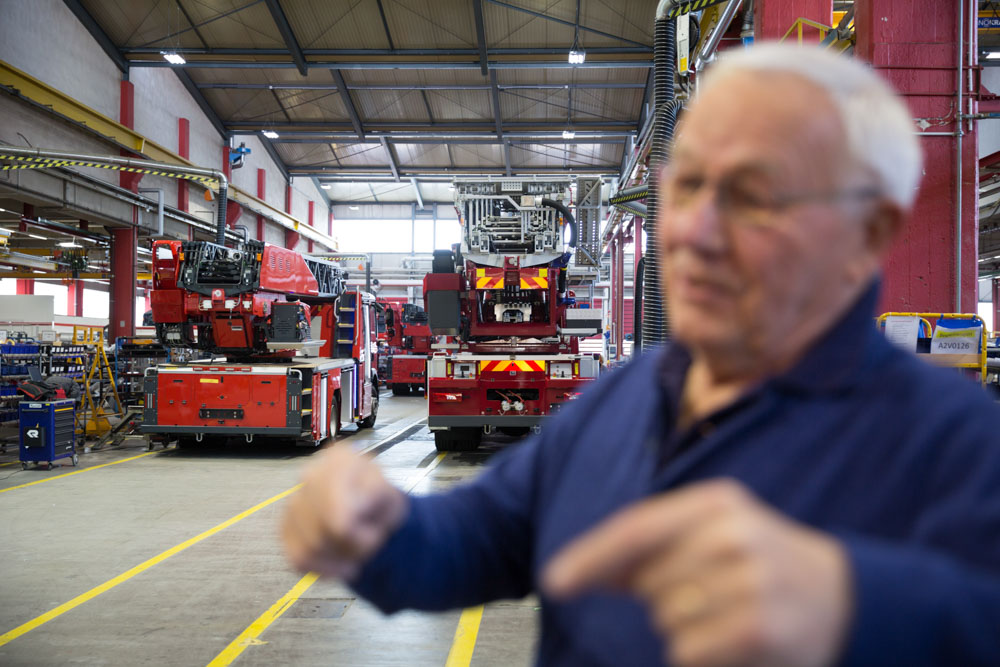 Armin Maiwald steht vor Feuerwehrwagen während er erklärt und gestikuliert. 
