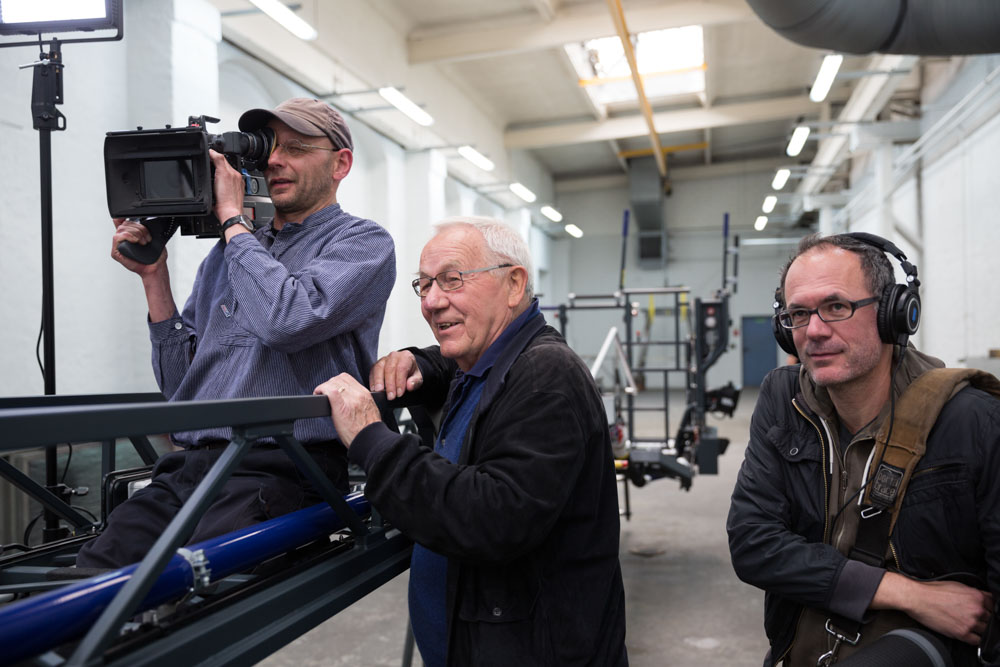Armin Maiwald steht neben seinem Filmteam und beobachtet die Dreharbeiten. 