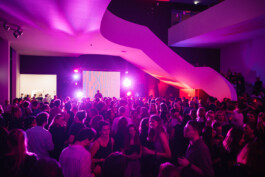 Eine große Anzahl an Menschen tanzt bei einer Veranstaltung auf einer bunt beleuchteten Tanzfläche. 