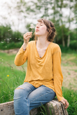 Portrait der Musikerin und Baubiologin Paula Töpper auf einer Wiese mit einer Pusteblume