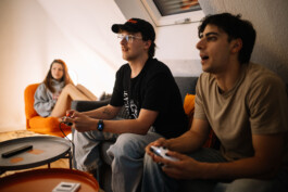 Hannes und Ali sitzen auf der Couch und konzentrieren sich auf ein Spiel auf einer Spielkonsole.