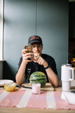 Hannes sitzt mit seinem Handy in der Küche vor einer Wassermelone.